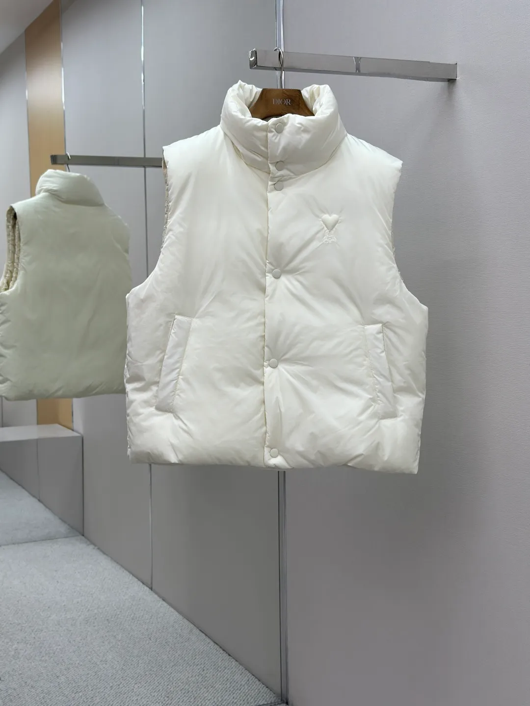 P810 AMIPARIS love padded embroidered down vest Fabric selection: Taffeta fabric woven from 100% polyester fiber. It adopts warp and weft plain weave and is woven very tightly, making the surface of the fabric extremely smooth and flat, with a "skinny" and stiffness that is not easy to collapse. When rubbed or moved around, it will make a unique, crisp "rustling" sound. At the same time, it has a delicate plain texture and a soft, elegant silky luster. This kind of luster is not as dazzling as satin, but more restrained and advanced.  Lining selection: Use 100% nylon to create the lining. The high-density and tight weaving process prevents tiny lint from getting out of the gaps in the fabric. The smooth surface improves the putting on and taking off experience, and the excellent wear and tear resistance ensures damage caused by frequent use, while the light and soft texture does not affect the overall weight.  Technology: The fabric and padding material are tightly fixed on the frame of the embroidery machine. The embroidery machine uses sparse stitches along the padding layer to outline the filling area of the pattern, and then runs the overlay layer's padding, using dense stitches to perfectly cover the foam padding layer, thus forming a slightly raised love embroidery, which feels soft and full, enhancing recognition while maintaining a low profile. High-quality filling: It uses 90 white duck down with a weight of 160g to ensure excellent thermal insulation performance. After strict screening and processing, the velvet is not easy to get drilled, ensuring durability.  Accessories: One-to-one customized three-standard, one-to-one customized hem elastic buckle, one-to-one customized snap button SIZE: XS S M L